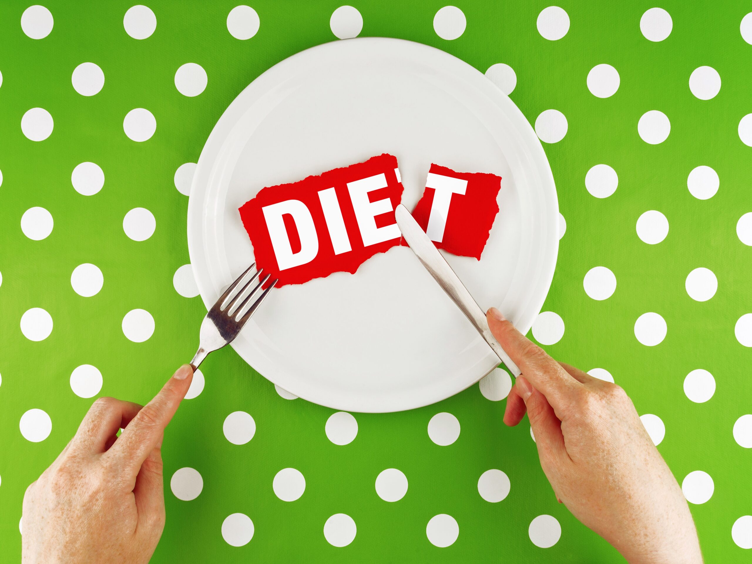 person holding a fork and knife, cutting into the word "diet" on a plate