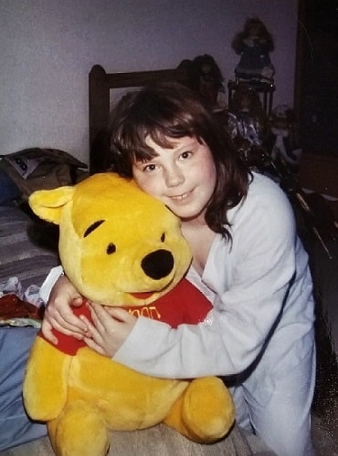 Anna, age 8, wearing white, long-sleeve pajamas while hugging a large Winnie the Pooh stuffed animal; in the early stages of learning to hate her body